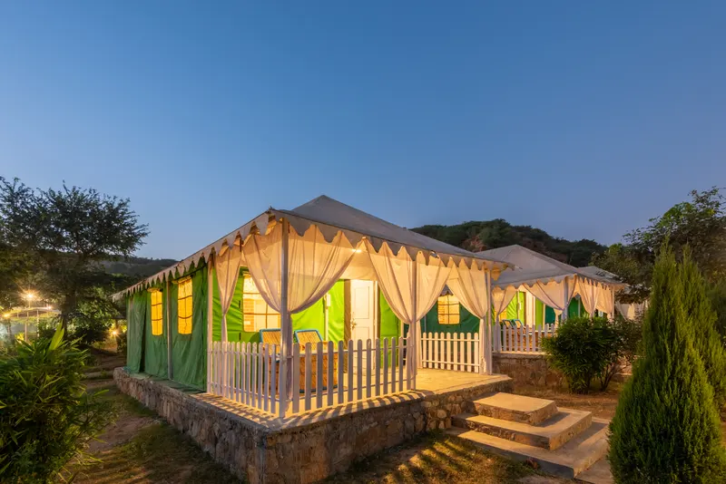 Jungle View Tents with illuminated verandas at dusk at Farm Aravalia