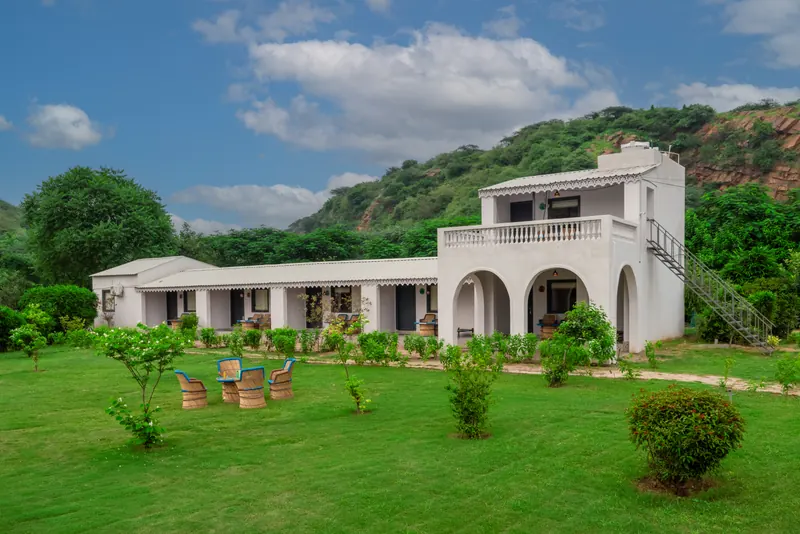 White retreat buildings and green lawns framed by the Aravalli hills